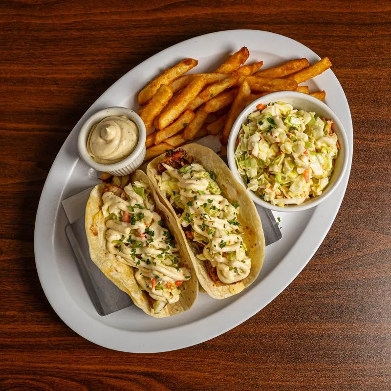 Grouper tacos drizzled with sauce, served with fries and coleslaw